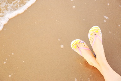 Photo of Closeup of woman with stylish flip flops on sand near sea, space for text. Beach accessories