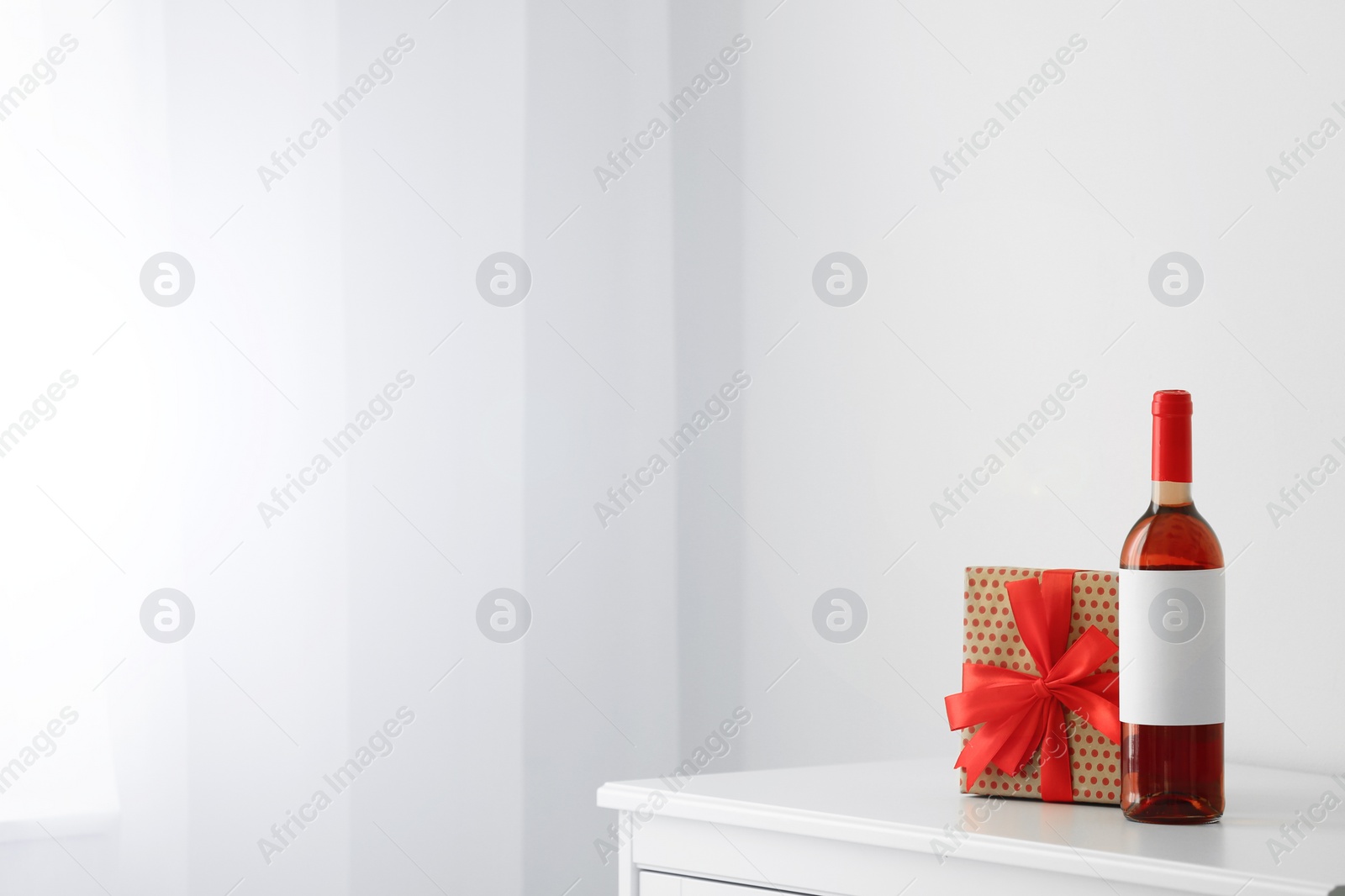 Photo of Bottle of wine and gift box on table in light room. Space for text