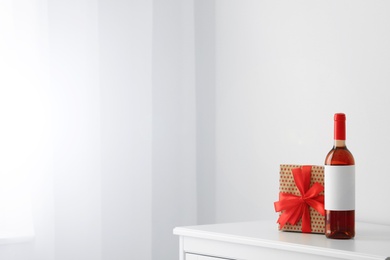 Photo of Bottle of wine and gift box on table in light room. Space for text