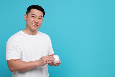Handsome man with jar of body cream on light blue background. Space for text
