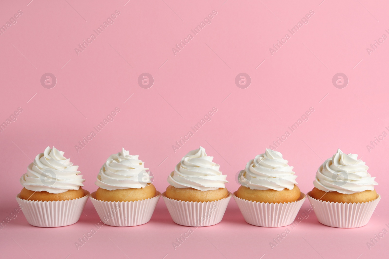Photo of Delicious cupcakes with white cream on pink background. Space for text