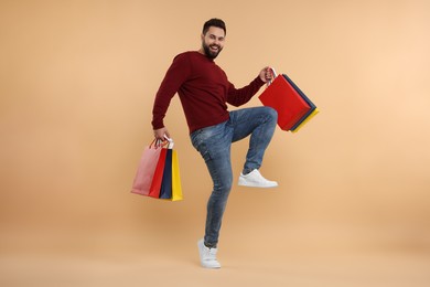 Photo of Happy man with many paper shopping bags on beige background