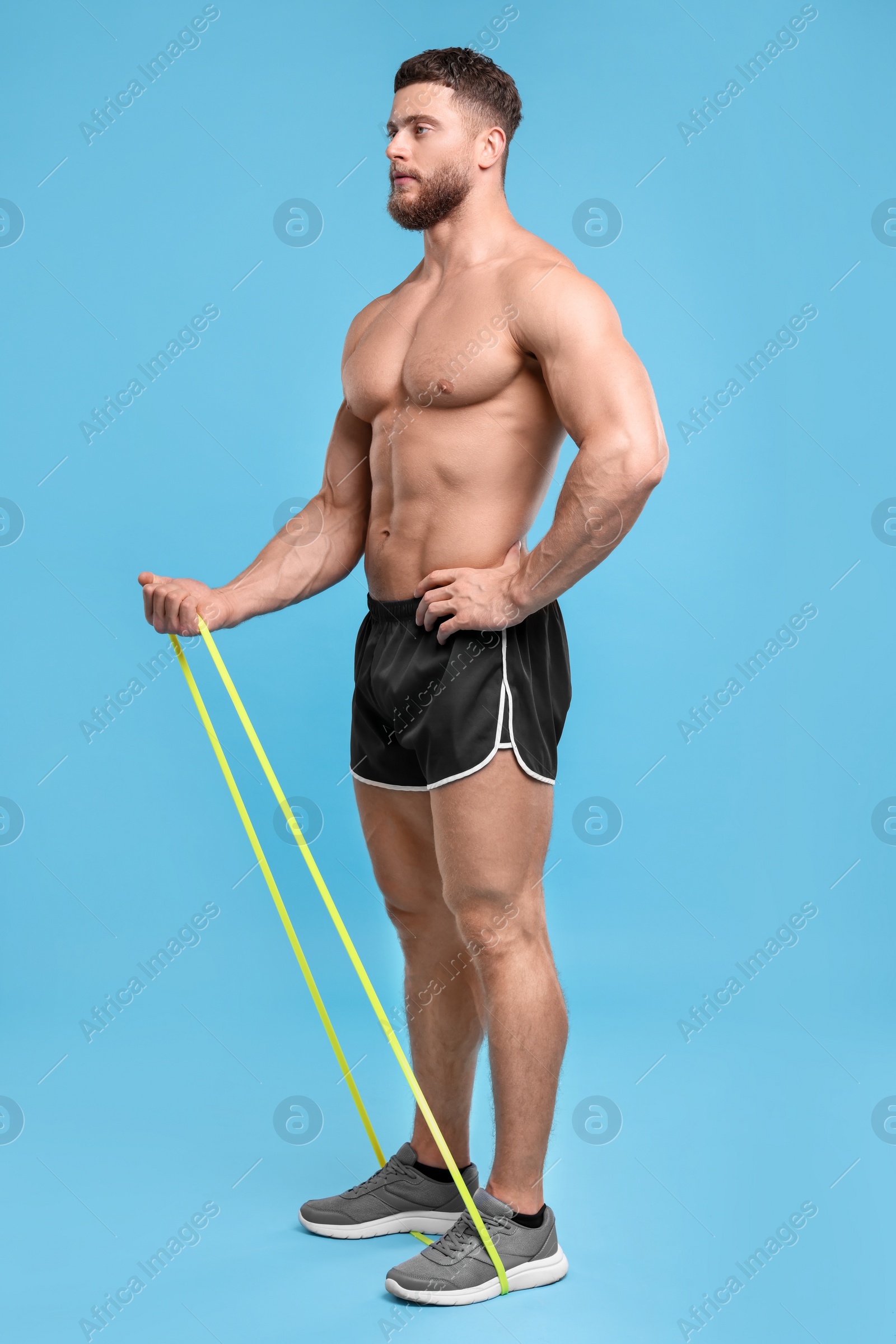 Photo of Young man exercising with elastic resistance band on light blue background