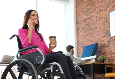 Photo of Young woman in wheelchair talking on smartphone at office