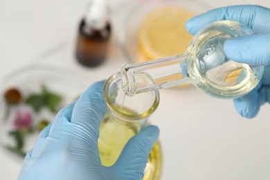 Scientist in medical gloves developing cosmetic oil, closeup view