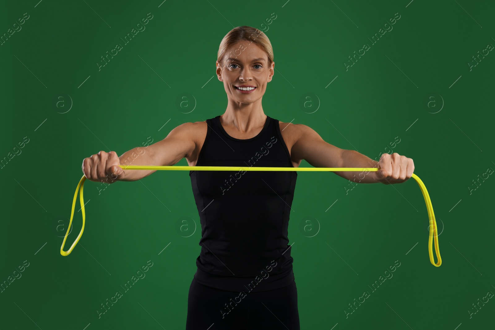 Photo of Smiling woman exercising with elastic resistance band on green background