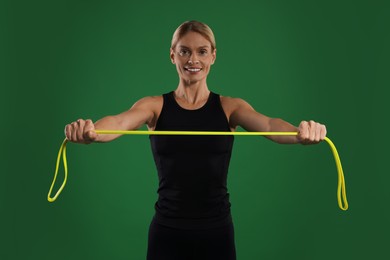 Smiling woman exercising with elastic resistance band on green background