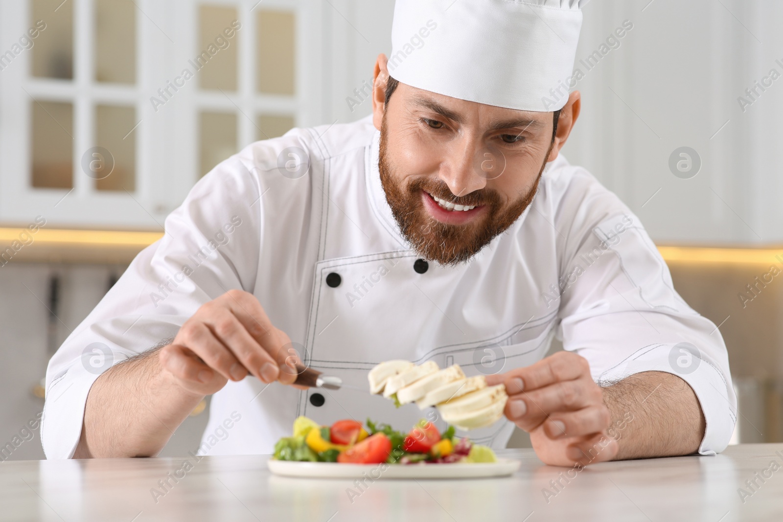 Photo of Professional chef adding mozzarella into delicious salad at marble table in kitchen