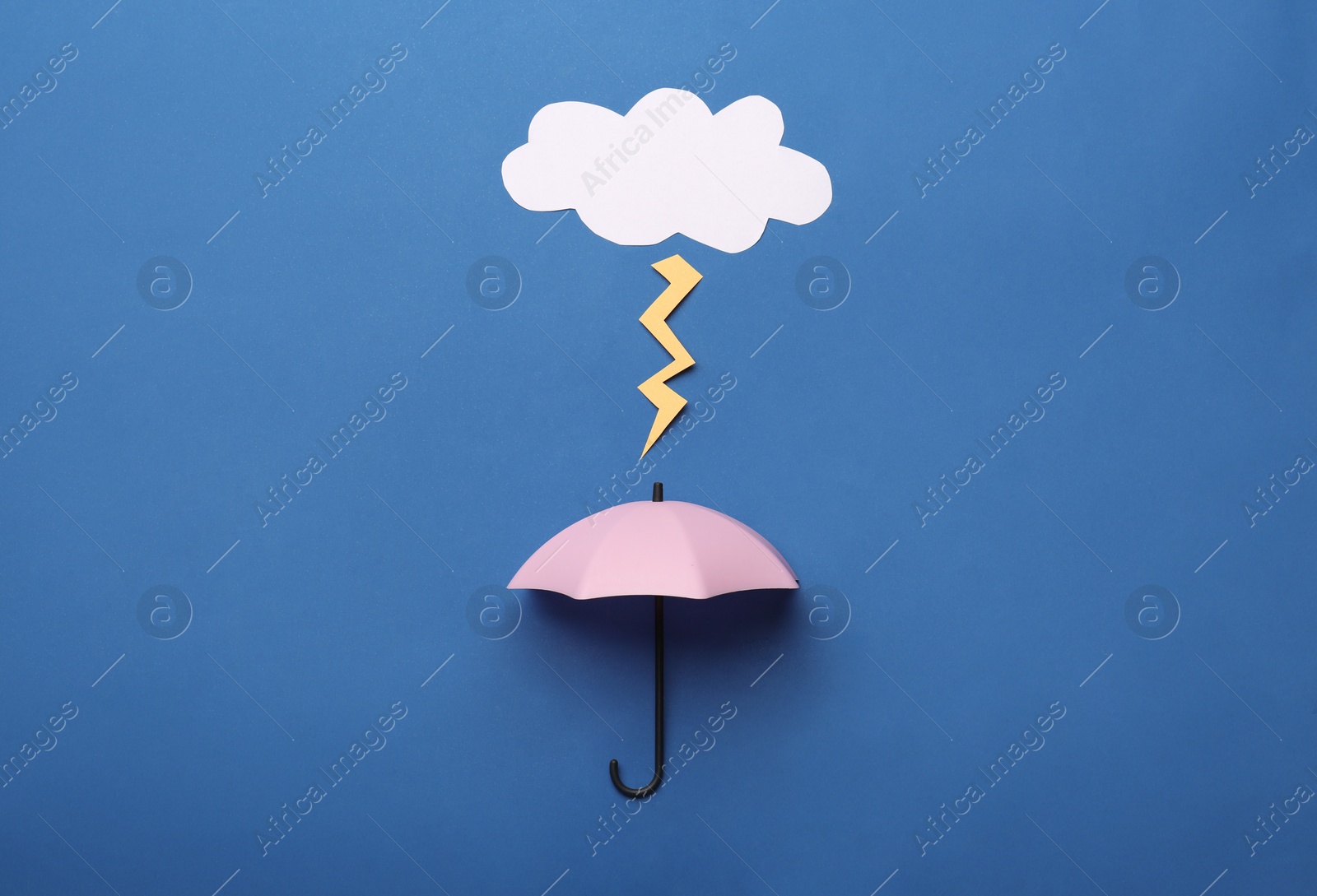 Photo of Mini umbrella and paper lighting cloud on blue background, flat lay