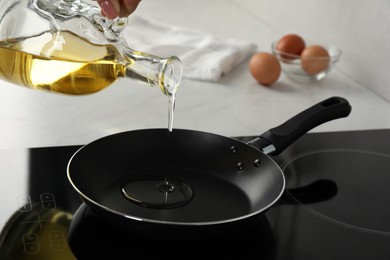 Woman pouring cooking oil from jug into frying pan on stove, closeup