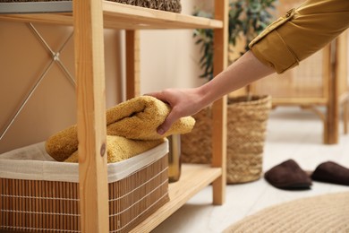 Photo of Woman putting towel into storage basket indoors, closeup