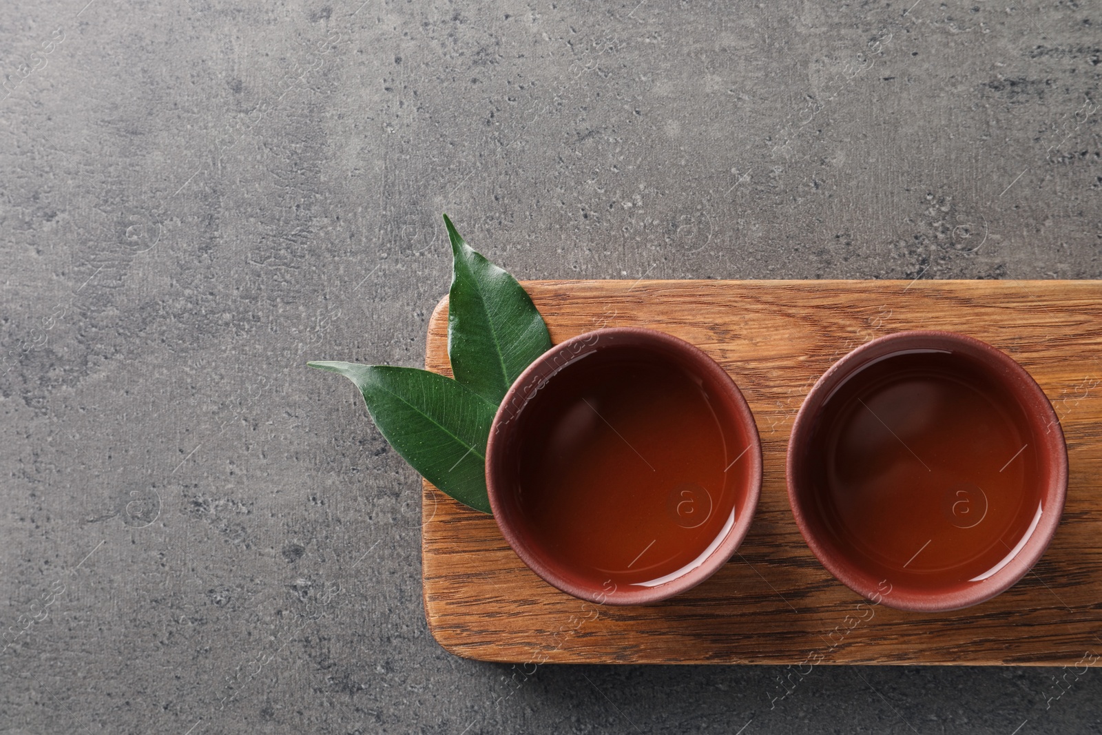 Photo of Board with cups of freshly brewed oolong tea on grey background, top view with space for text