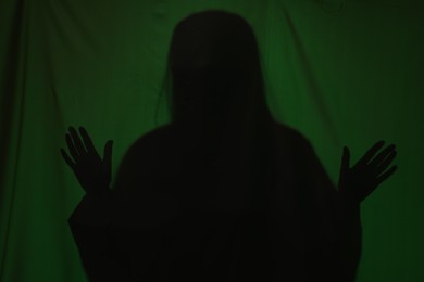 Silhouette of creepy ghost behind dark green cloth