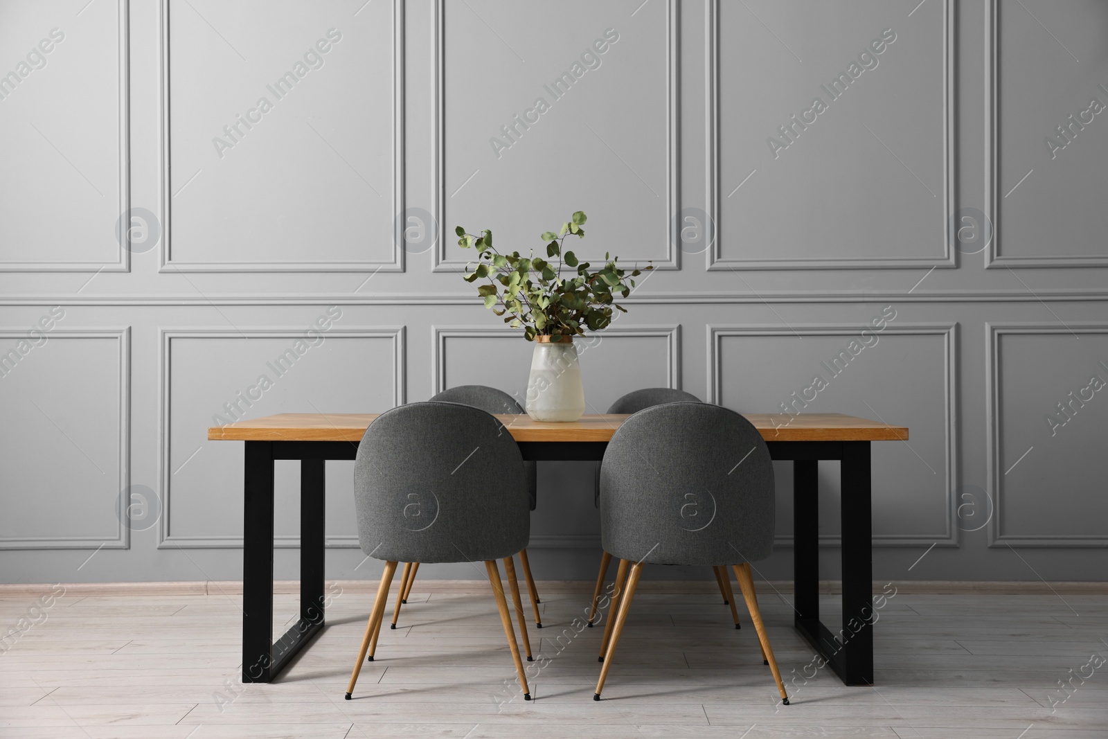 Photo of Soft chairs, table and vase with eucalyptus branches in stylish dining room