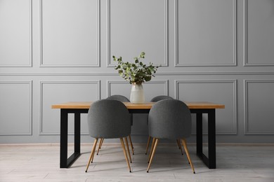 Photo of Soft chairs, table and vase with eucalyptus branches in stylish dining room