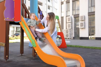 Photo of Happy nanny and cute little boy on slide outdoors