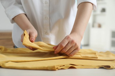 Woman folding clothes at white wooden table indoors, closeup