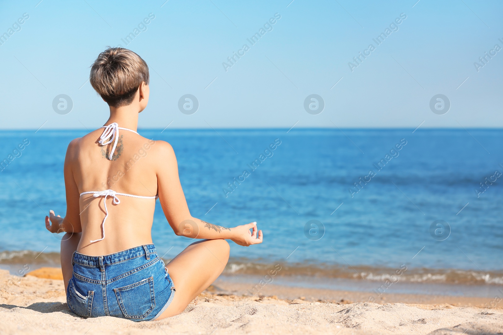 Photo of Young woman meditating on beach. Space for text