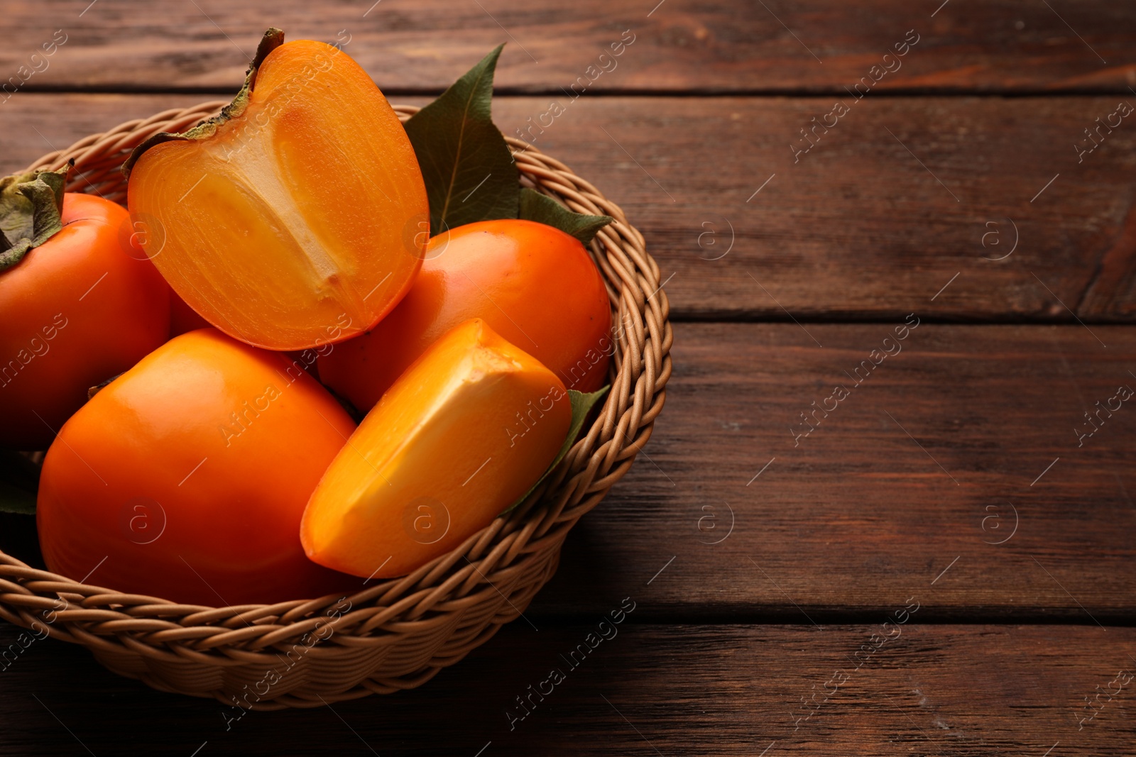 Photo of Delicious ripe persimmons in wicker basket on wooden table, space for text