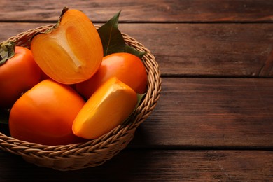 Photo of Delicious ripe persimmons in wicker basket on wooden table, space for text