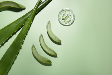 Photo of Cut aloe vera leaves and cosmetic gel on light green background, flat lay. Space for text