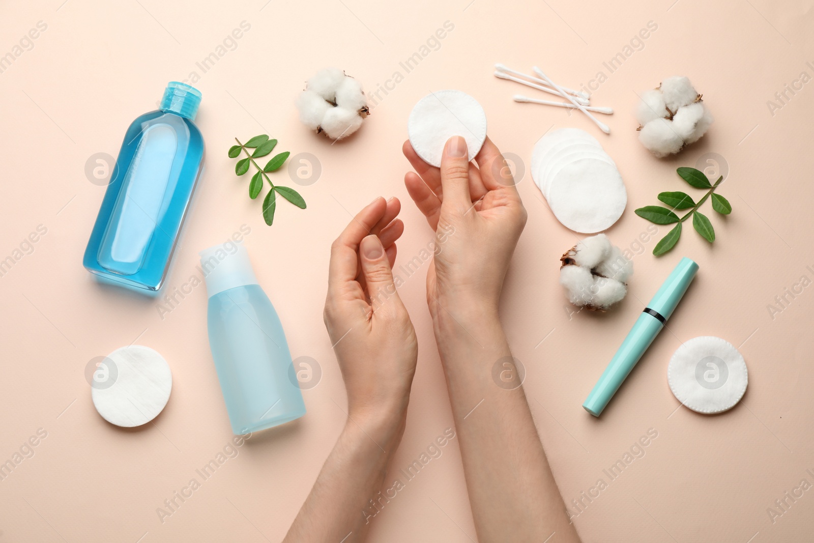 Photo of Woman holding cotton pad near makeup removal products on beige background, top view