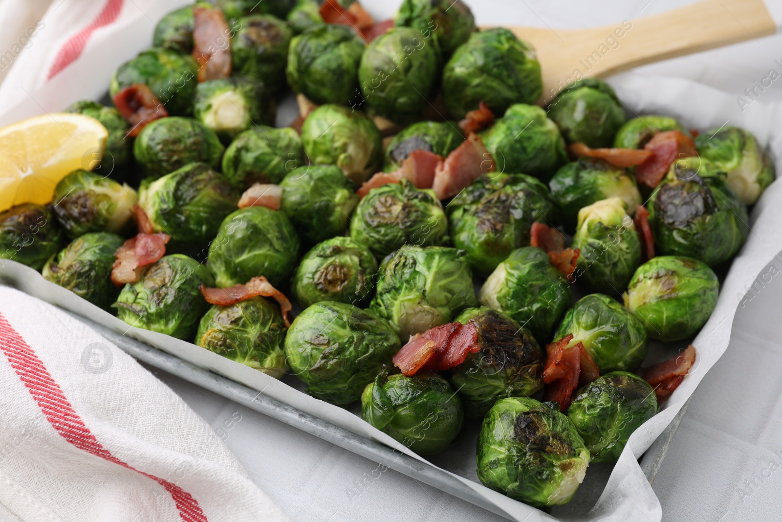 Photo of Delicious roasted Brussels sprouts, bacon and lemon in baking dish on white tiled table, closeup