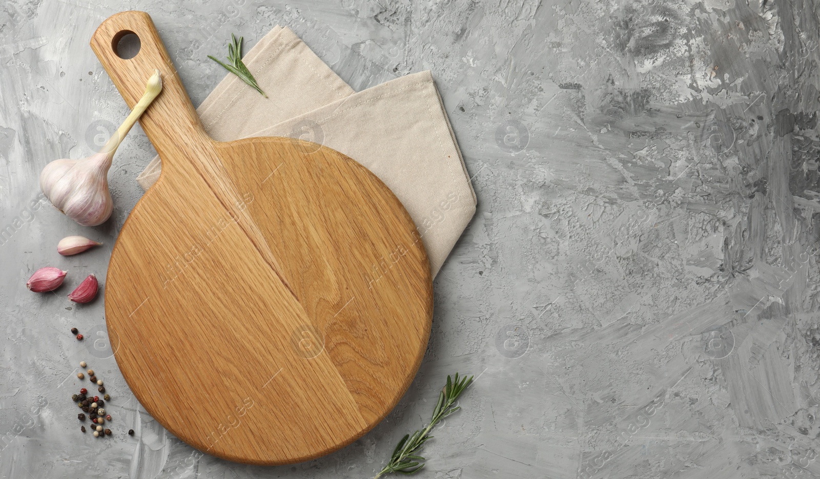 Photo of Cutting board, garlic, spices and rosemary on grey textured table, flat lay. Space for text