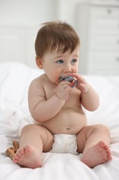 Cute baby boy with pacifier and wooden rattle on bed at home