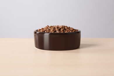 Dry dog food in pet bowl on wooden surface