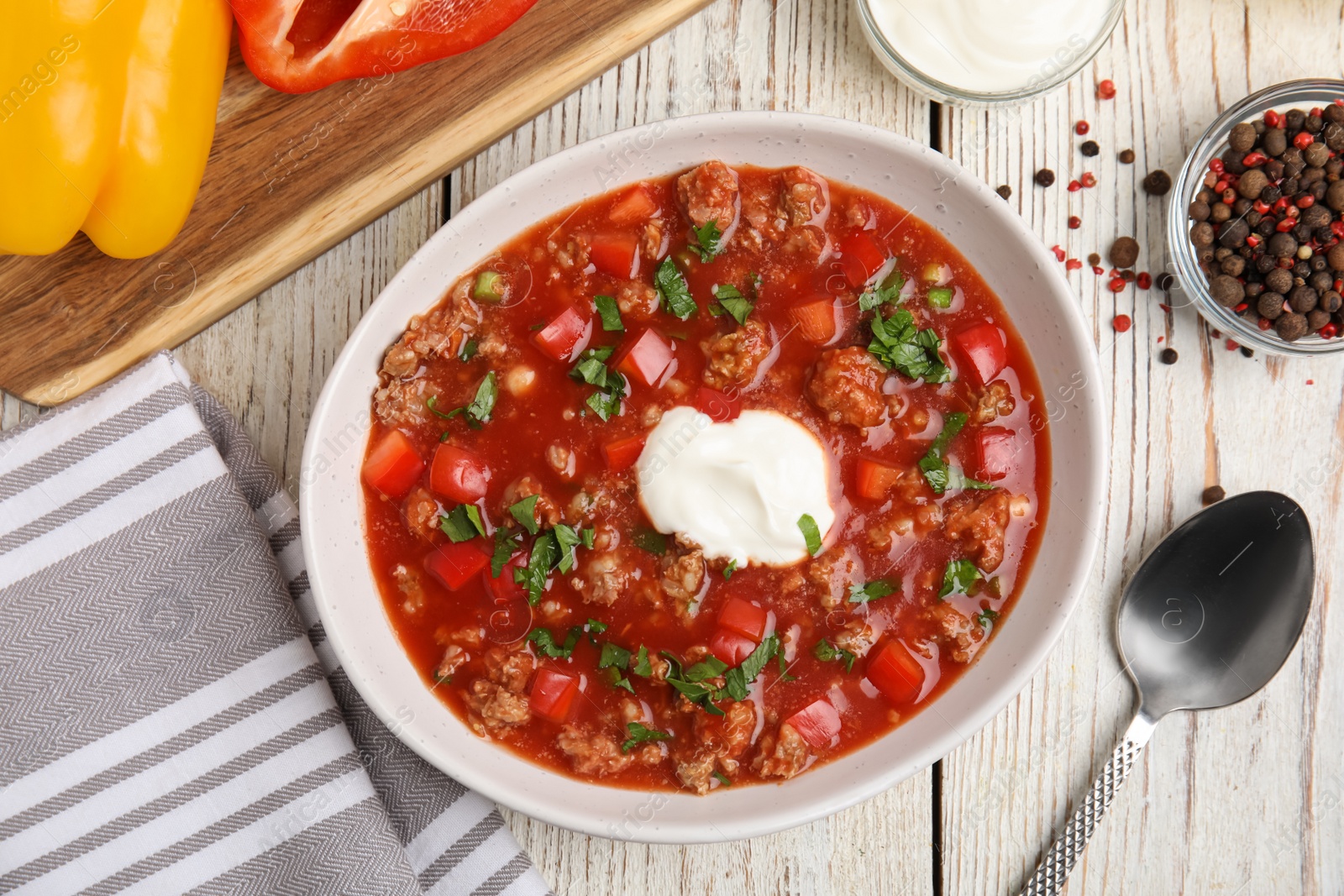 Photo of Bowl of delicious stuffed pepper soup on white wooden table, flat lay