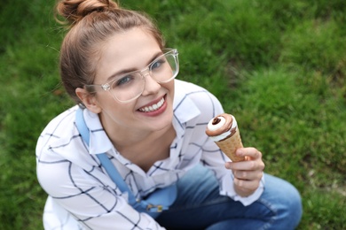 Photo of Young happy woman with ice cream cone sitting on grass in park