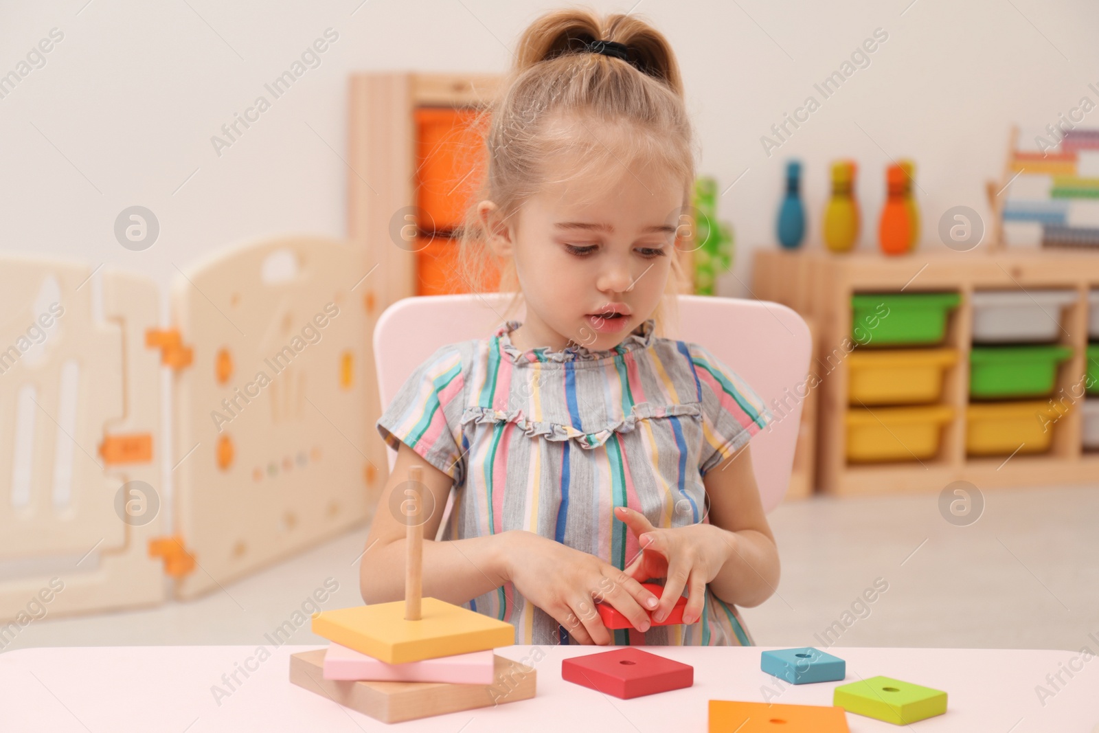 Photo of Cute child playing with colorful wooden stacker at table in room