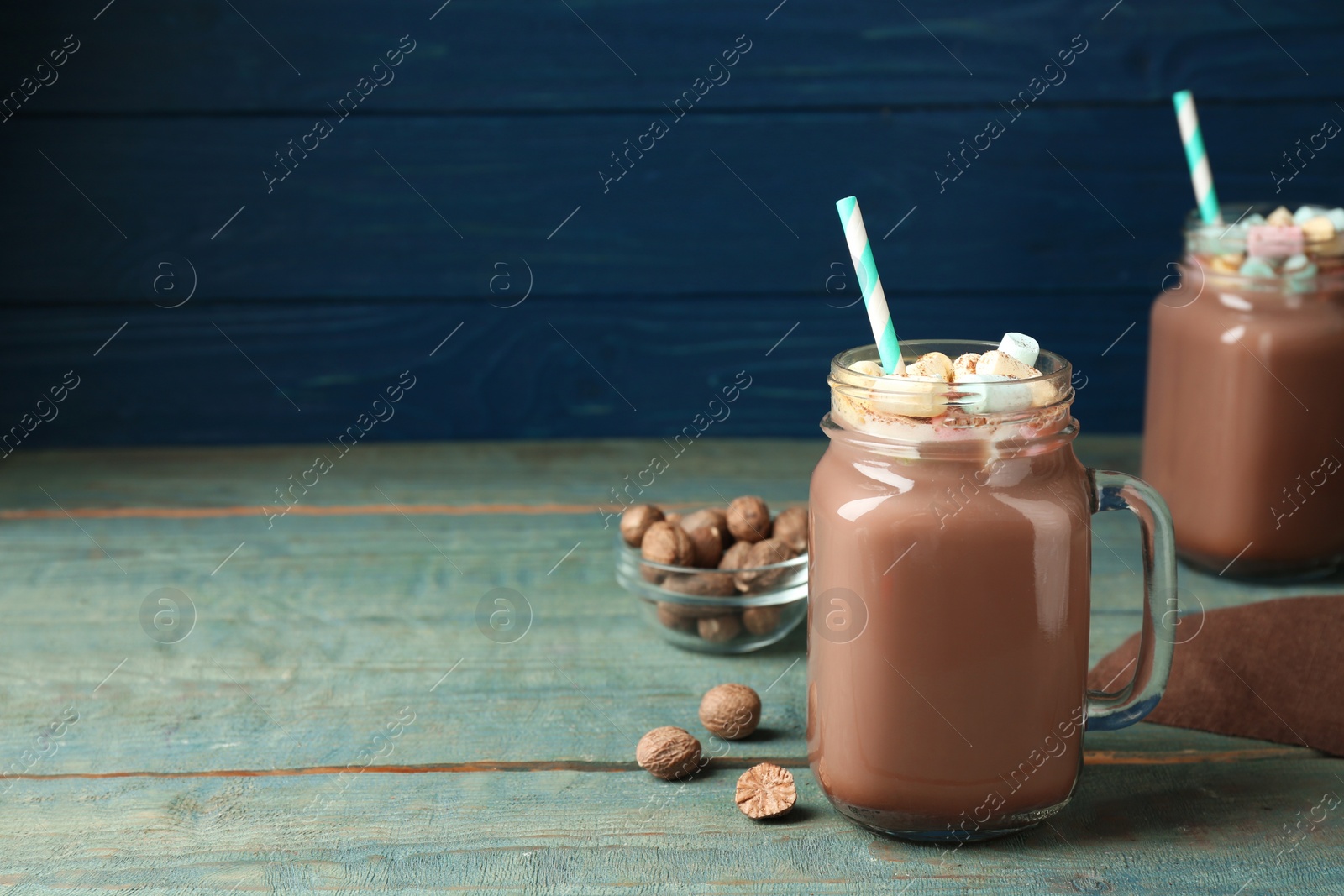 Photo of Hot drink with marshmallows and nutmeg powder on blue wooden table. Space for text