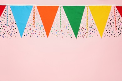Bunting with colorful triangular flags and other festive decor on pink background, flat lay. Space for text