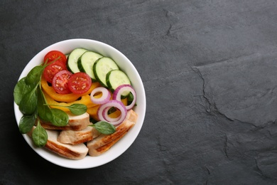 Photo of Delicious salad with chicken, vegetables and spinach  on black table, top view. Space for text