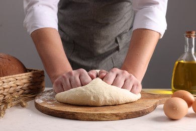 Photo of Man kneading dough at table near grey wall, closeup