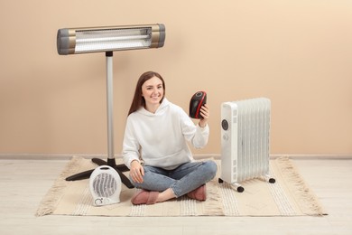 Photo of Young woman with different modern electric heaters near beige wall indoors