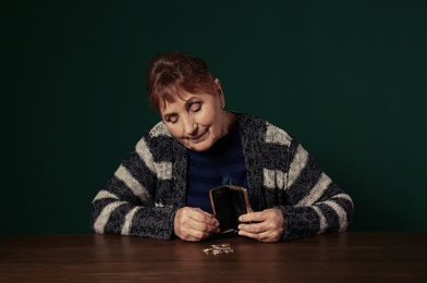 Poor senior woman with empty wallet and coins at table against color background