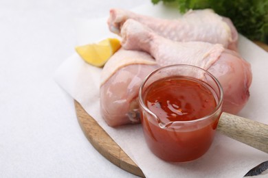 Photo of Fresh marinade and raw chicken drumsticks on white table, closeup. Space for text