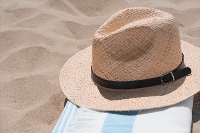 Photo of Straw hat and beach towel on sand, closeup. Space for text