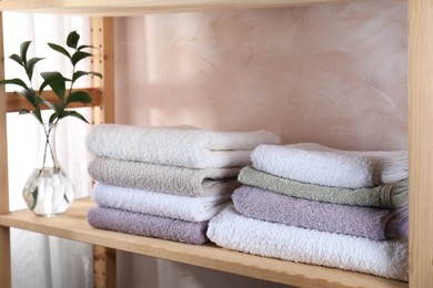 Photo of Stacked soft towels and green leaves on wooden shelf indoors