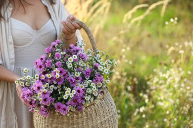 Photo of Woman holding wicker basket with beautiful wild flowers outdoors, closeup. Space for text