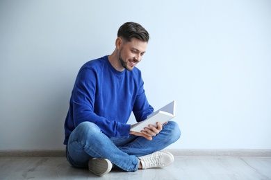 Handsome man reading book on floor near wall, space for text