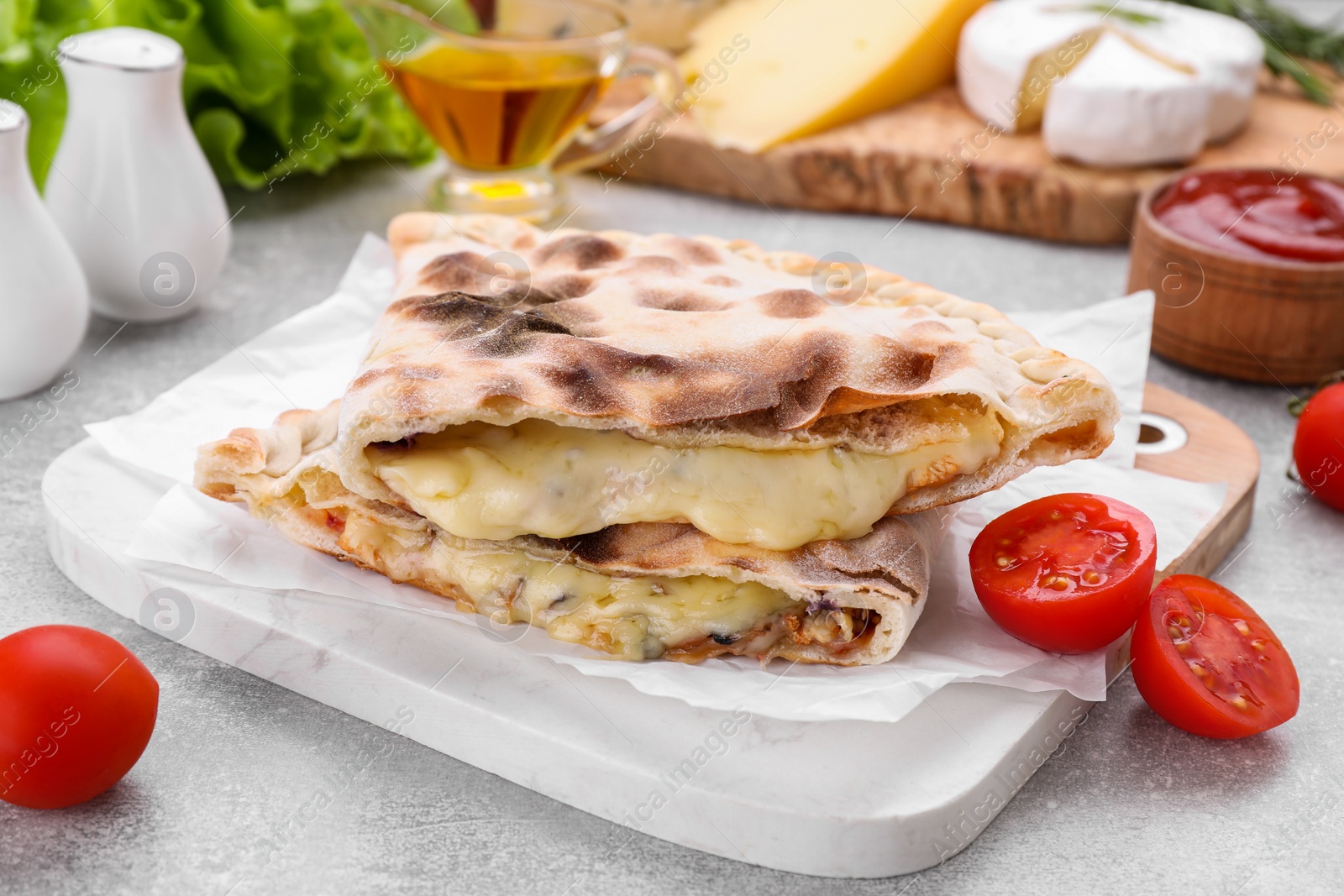 Photo of Tasty pizza calzones with cheese, tomato and different products on light grey table, closeup