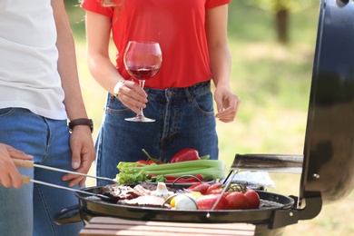 Photo of Young couple having barbecue with modern grill outdoors