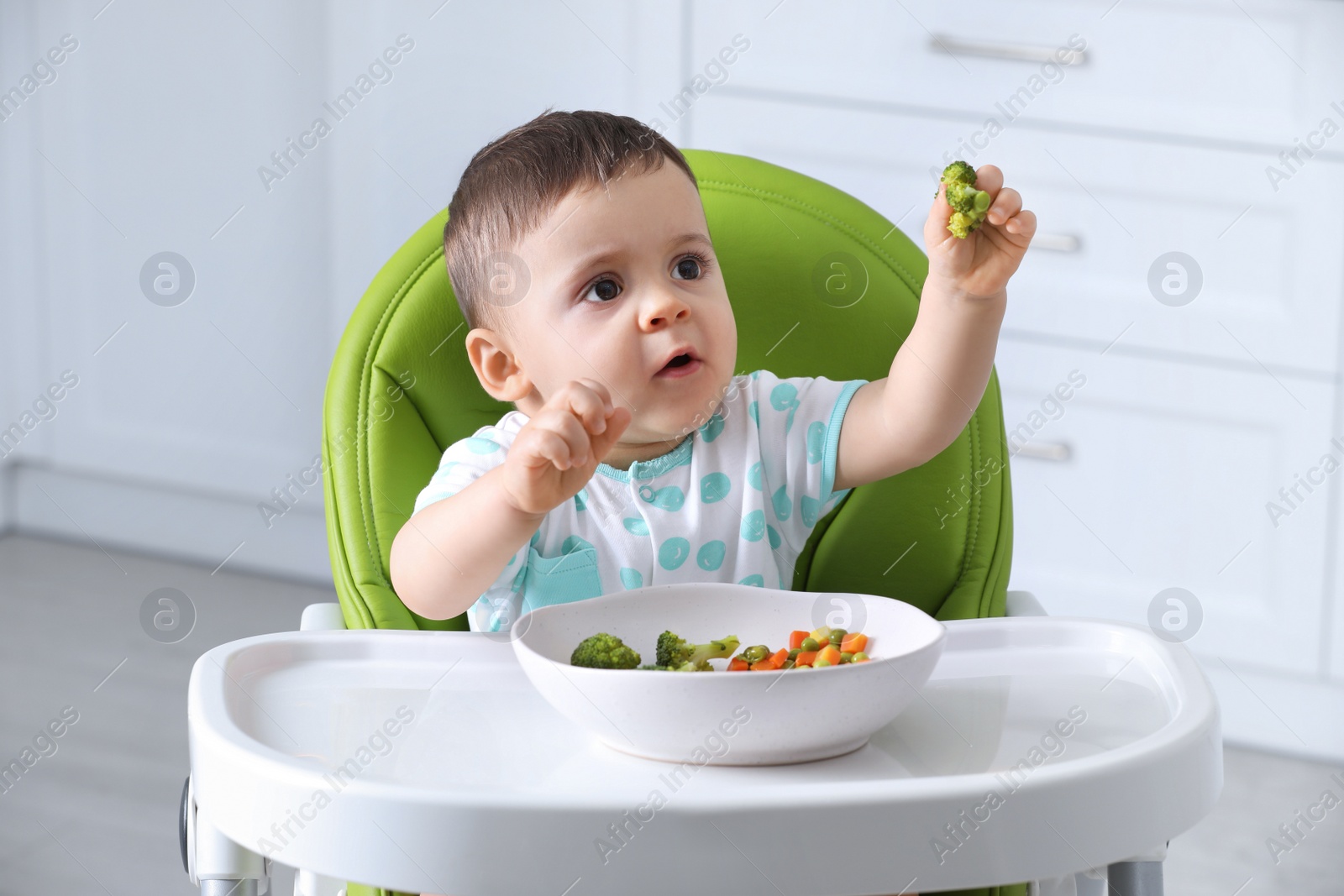 Photo of Cute little baby eating healthy food in high chair at home