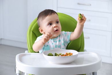 Cute little baby eating healthy food in high chair at home