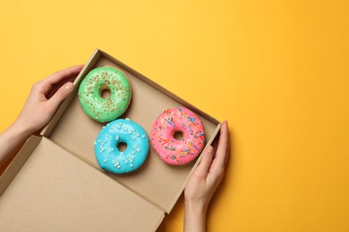 Woman with box of delicious donuts on yellow background, top view. Space for text