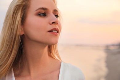 Photo of Beautiful young woman near sea at sunset, closeup. Space for text